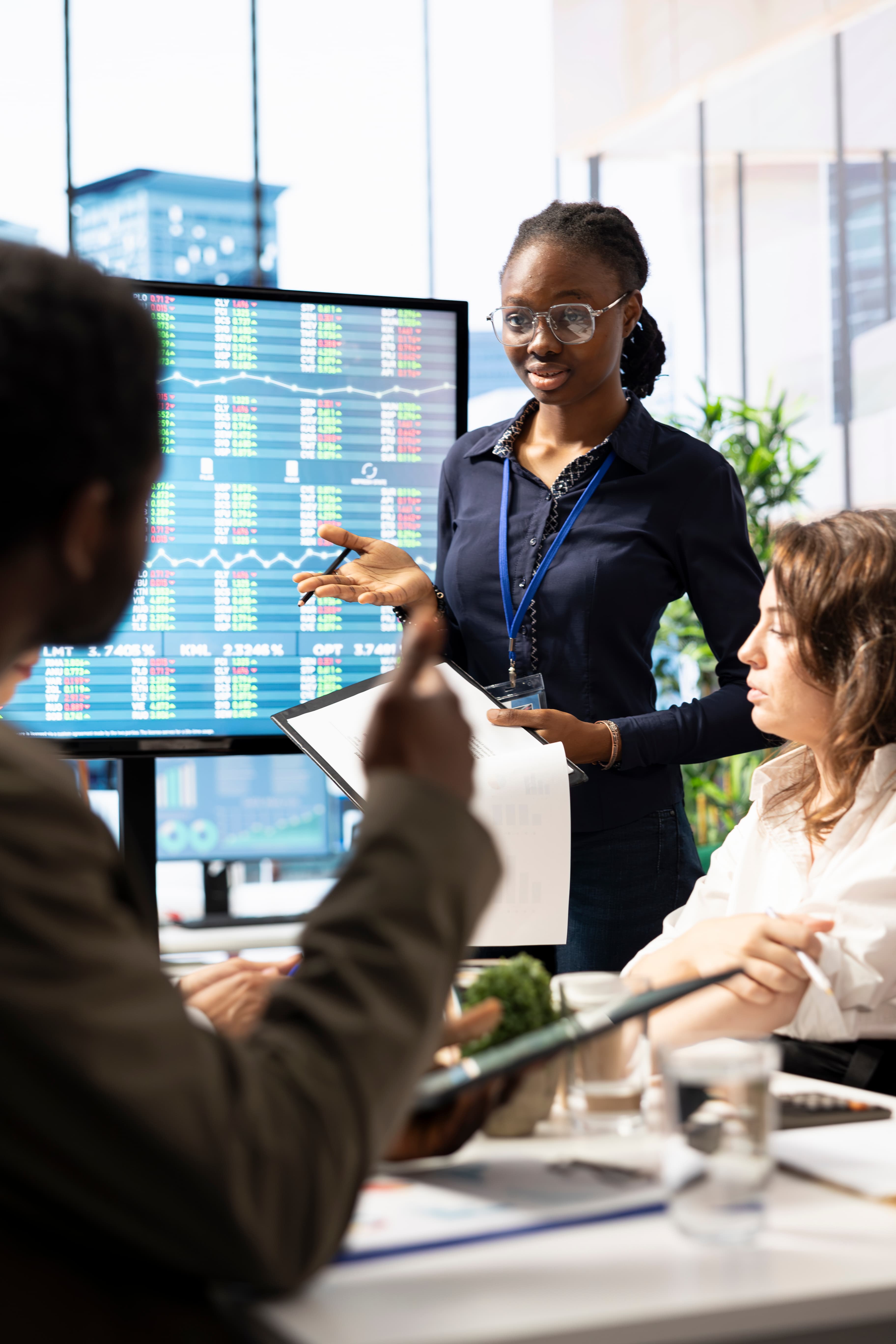 A presenter briefing colleagues in a boardroom in front of a live data screen.